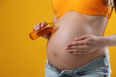 Photo of Young pregnant woman with sun protection oil on yellow background, closeup. Space for text