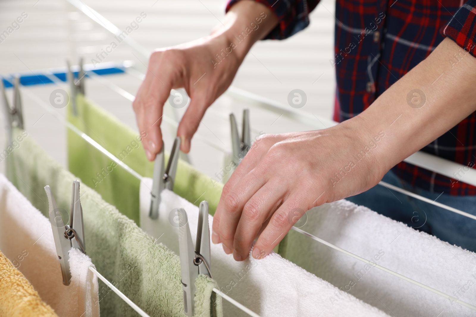 Photo of Woman hanging clean terry towels on drying rack indoors, closeup