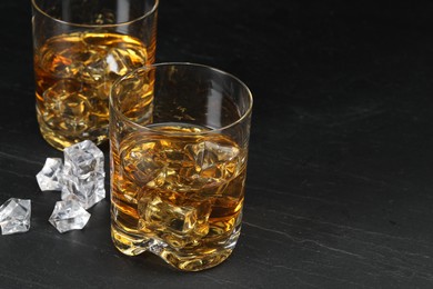 Whiskey and ice cubes in glasses on black table, closeup. Space for text