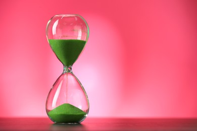 Photo of Hourglass with flowing green sand on table against pink background, space for text