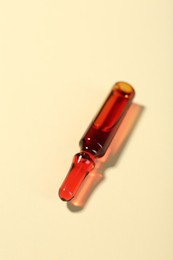 Photo of Glass ampoule with liquid on beige background