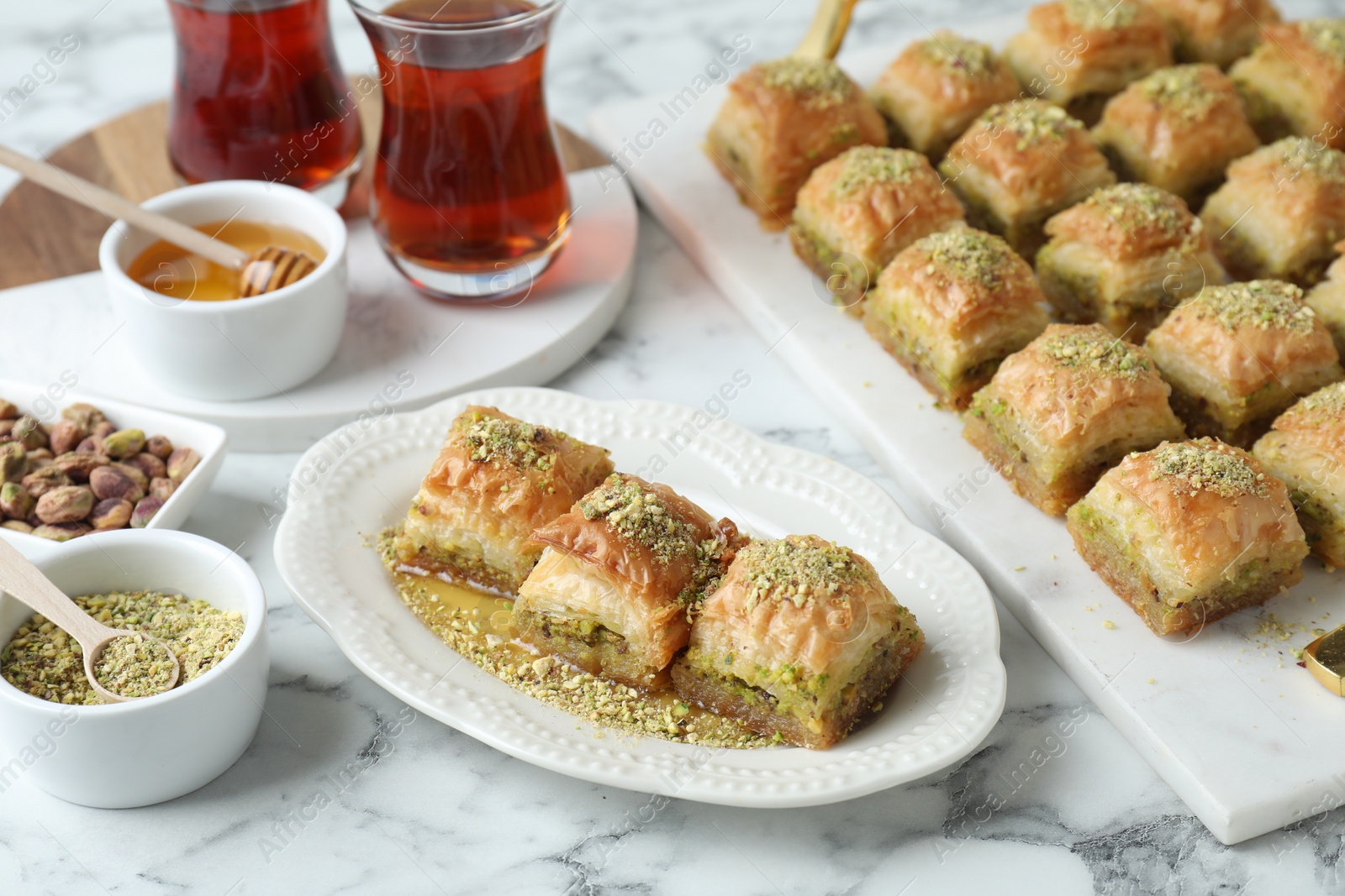 Photo of Delicious fresh baklava with chopped nuts and honey served on white marble table. Eastern sweets