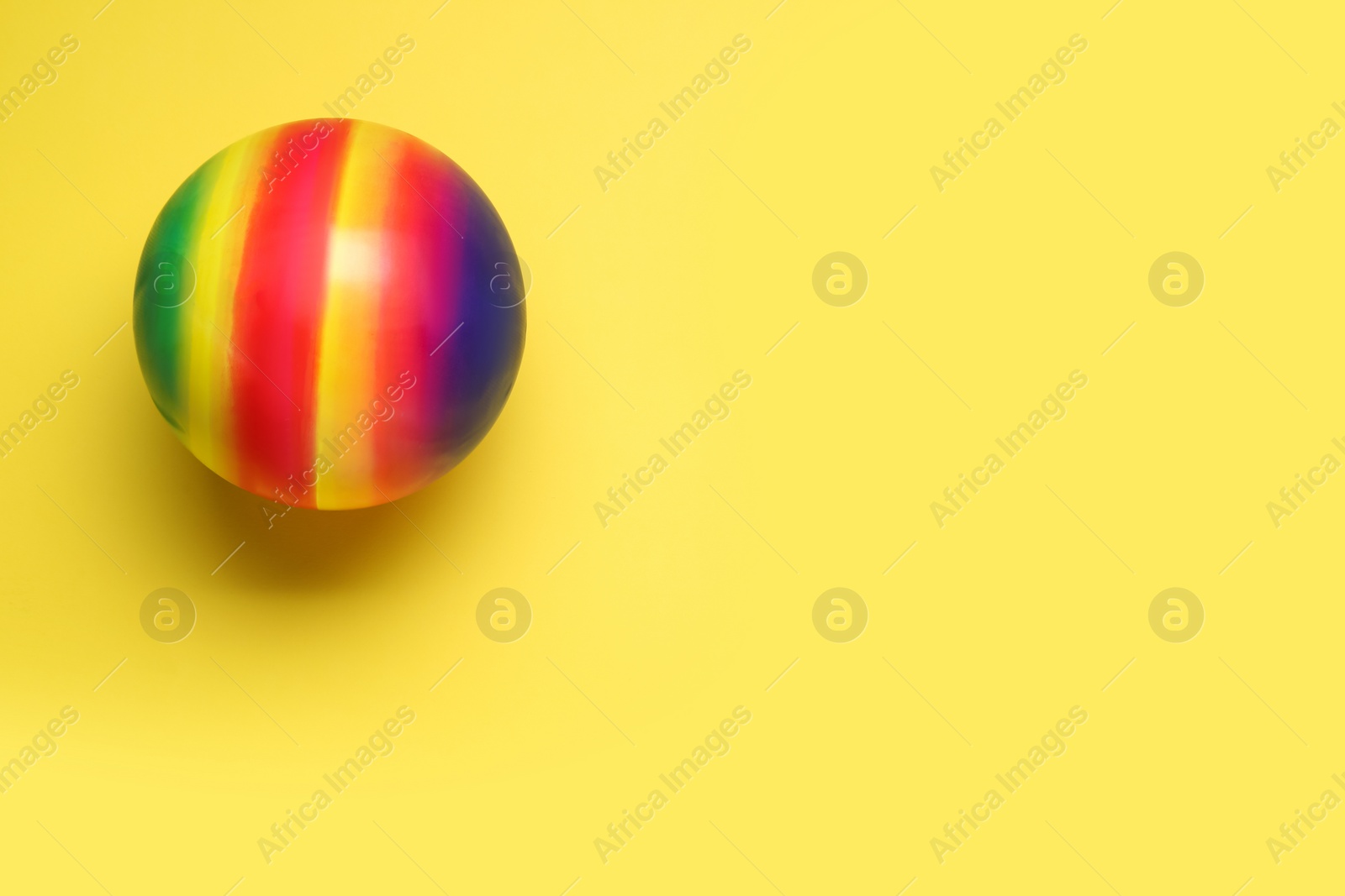 Photo of Bright rubber kids' ball on pale yellow background, top view. Space for text