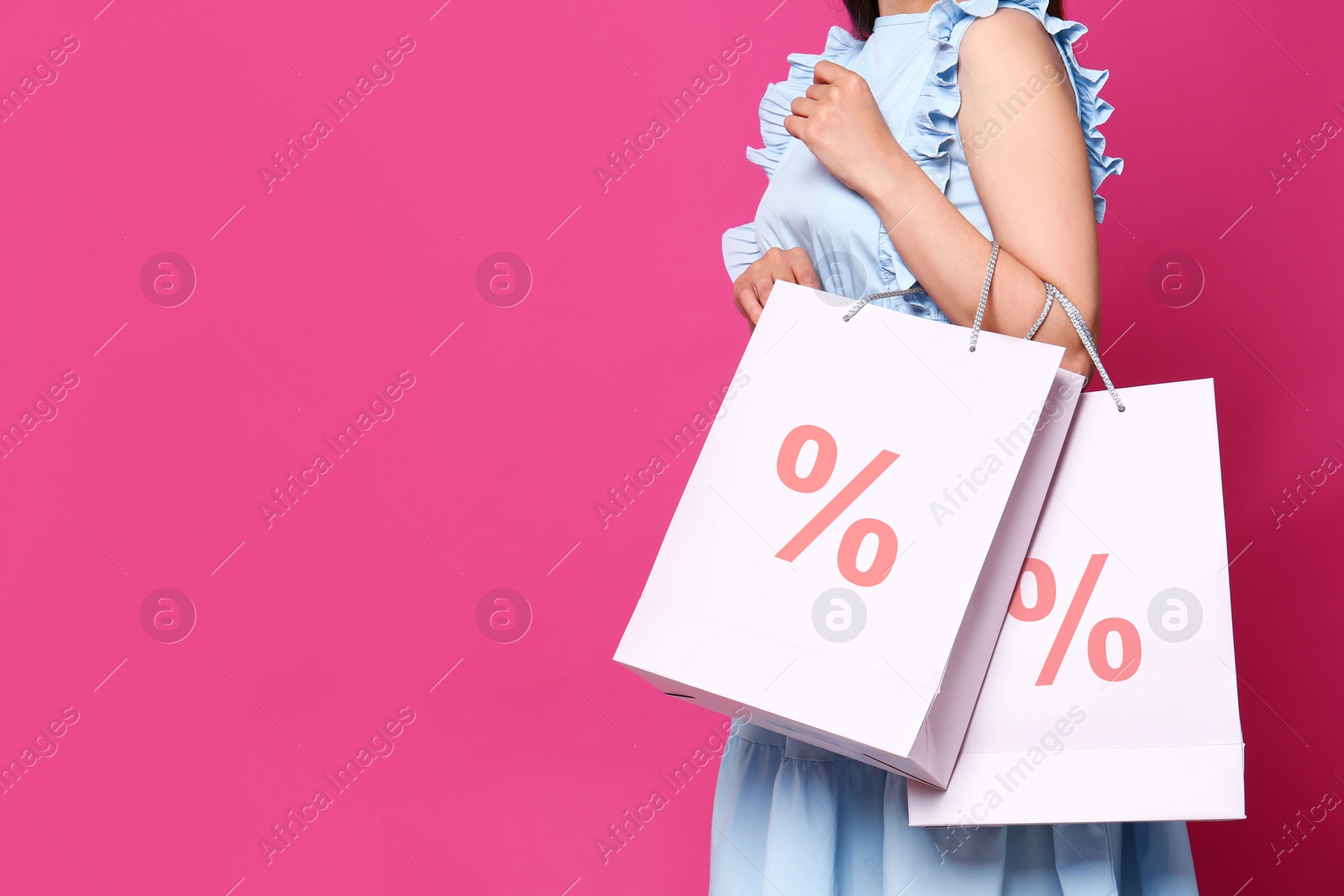 Image of Discount, sale, offer. Woman holding paper bags with percent signs against pink background, closeup. Space for text