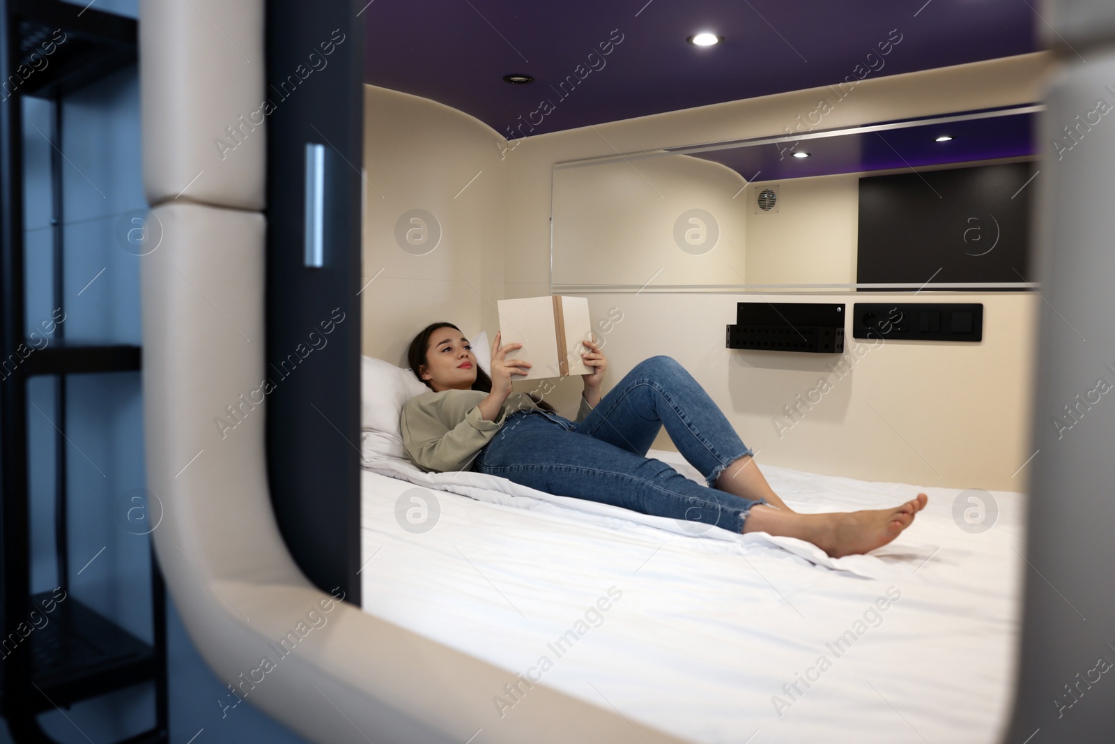 Photo of Young woman reading book in capsule of pod hostel