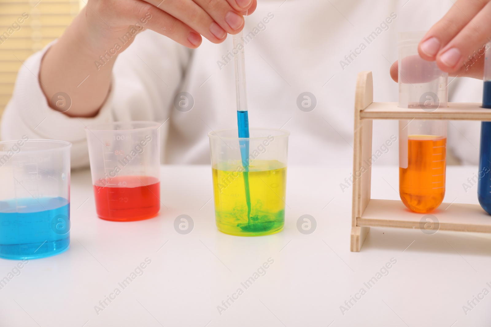 Photo of Girl mixing colorful liquids at white table indoors, closeup. Chemical experiment set for kids