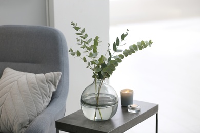 Photo of Vase with fresh eucalyptus branches on table in living room. Interior design