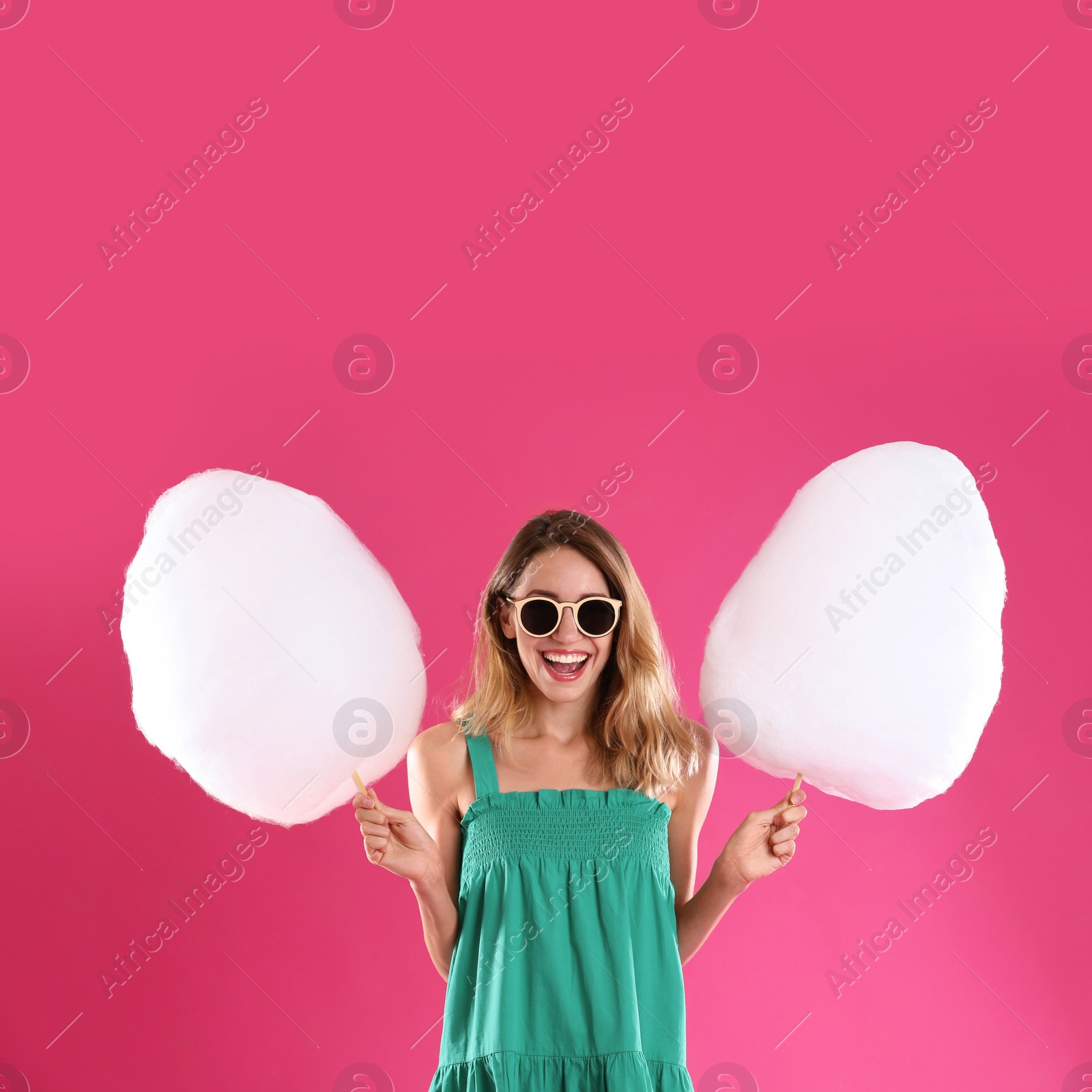 Photo of Happy young woman with cotton candies on pink background