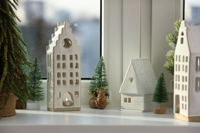 Beautiful house shaped candle holders and small fir trees on windowsill indoors