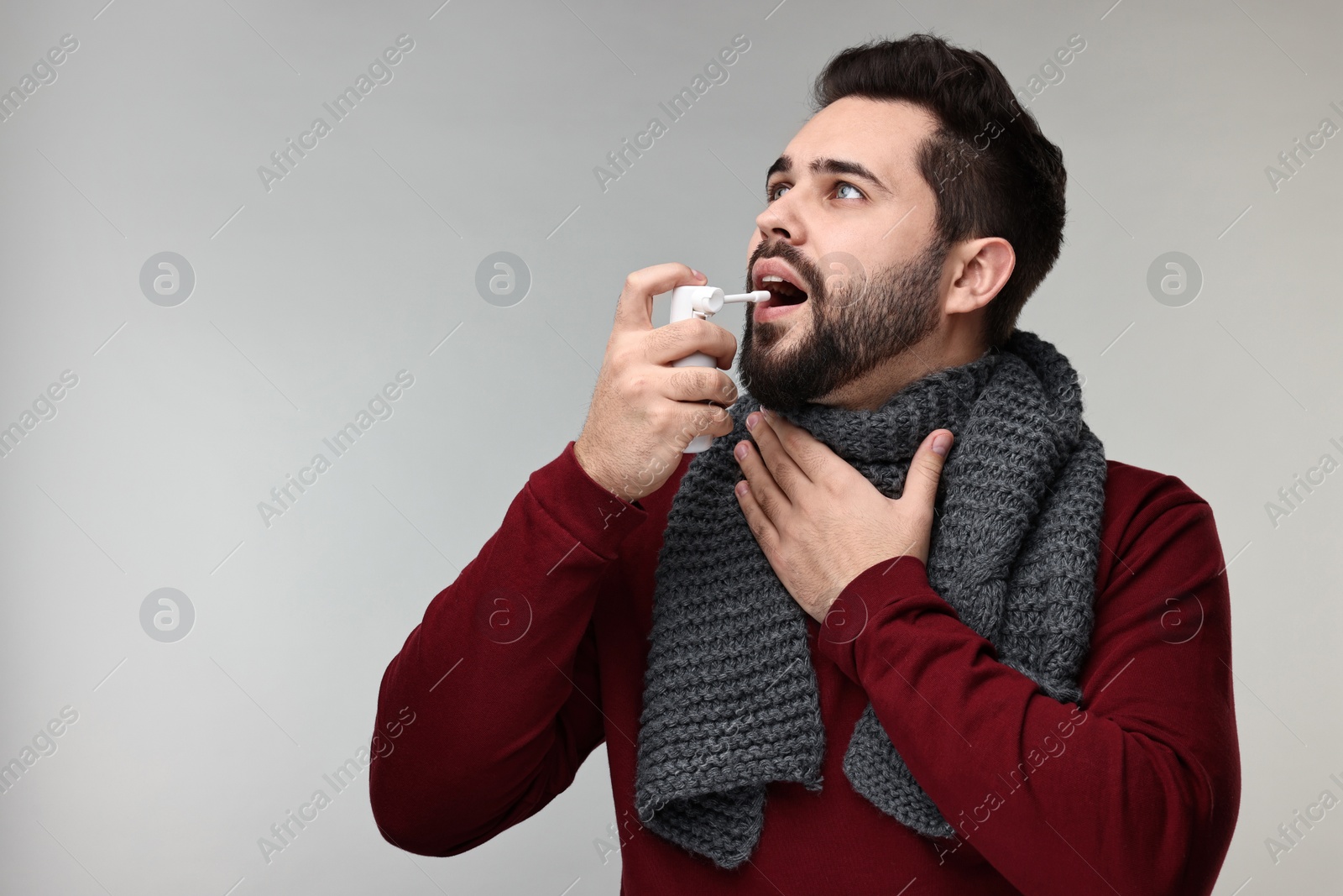 Photo of Young man with scarf using throat spray on grey background