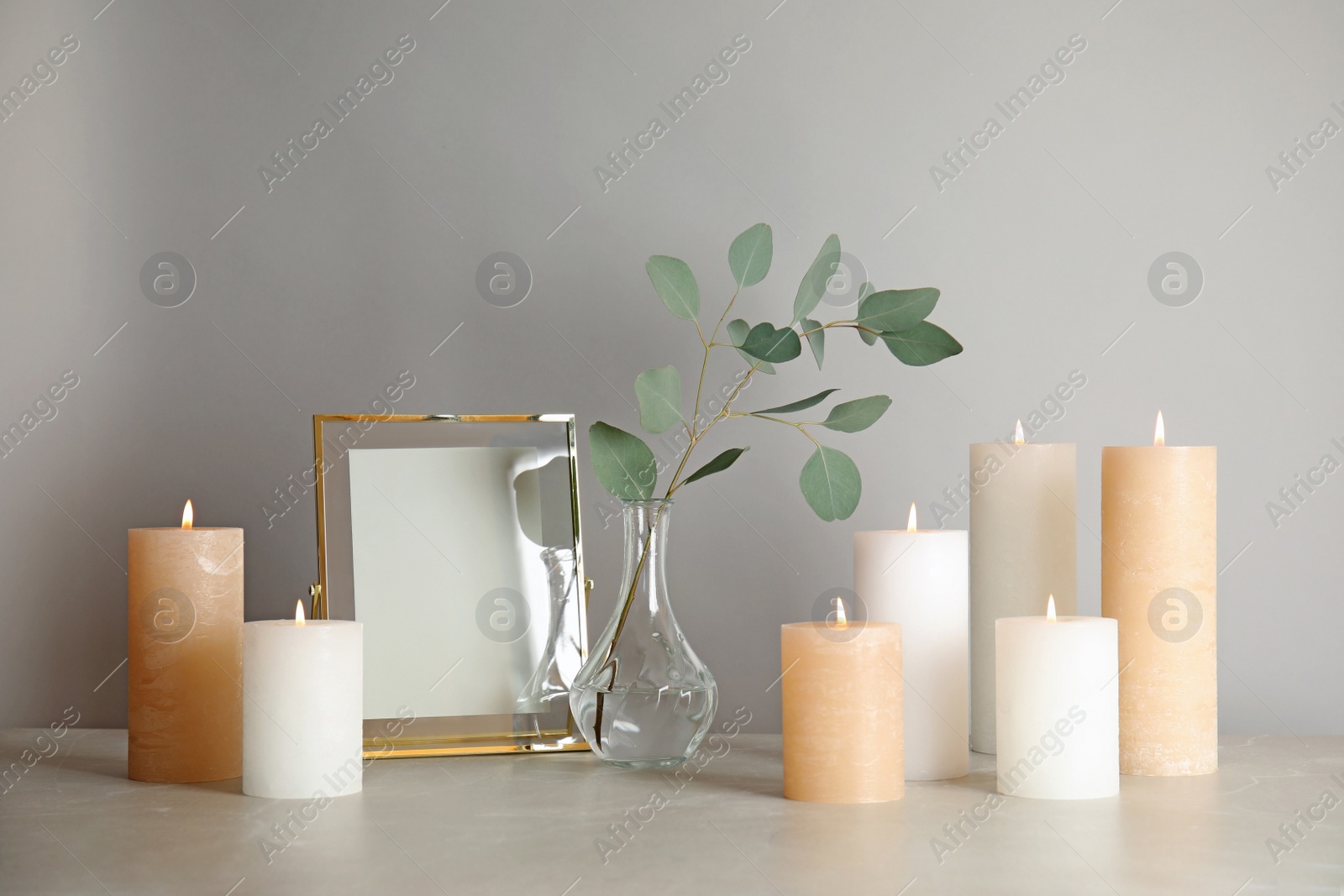 Photo of Composition with burning candles on table against light background