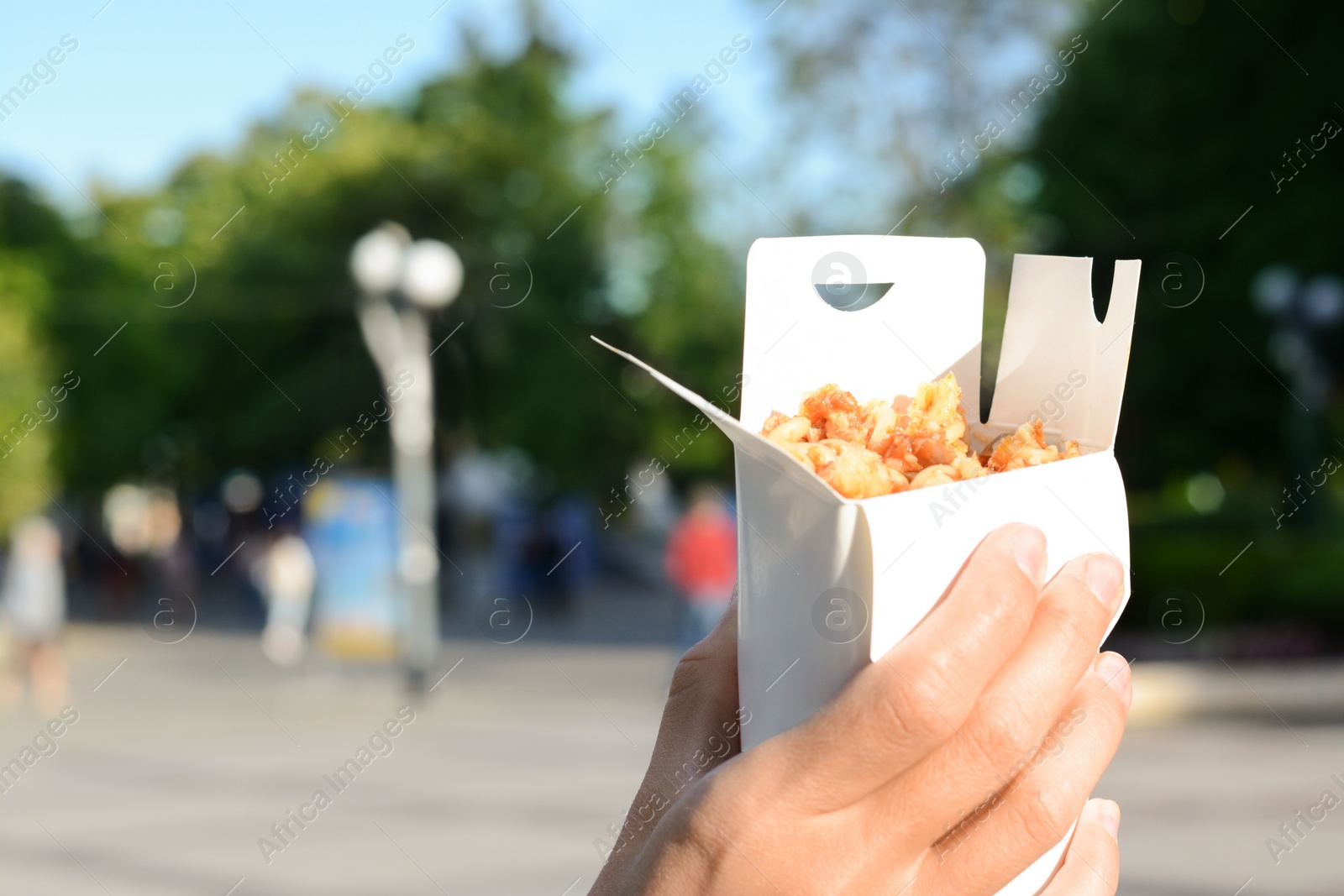 Photo of Woman holding paper box with takeaway noodles outdoors, closeup and space for text. Street food