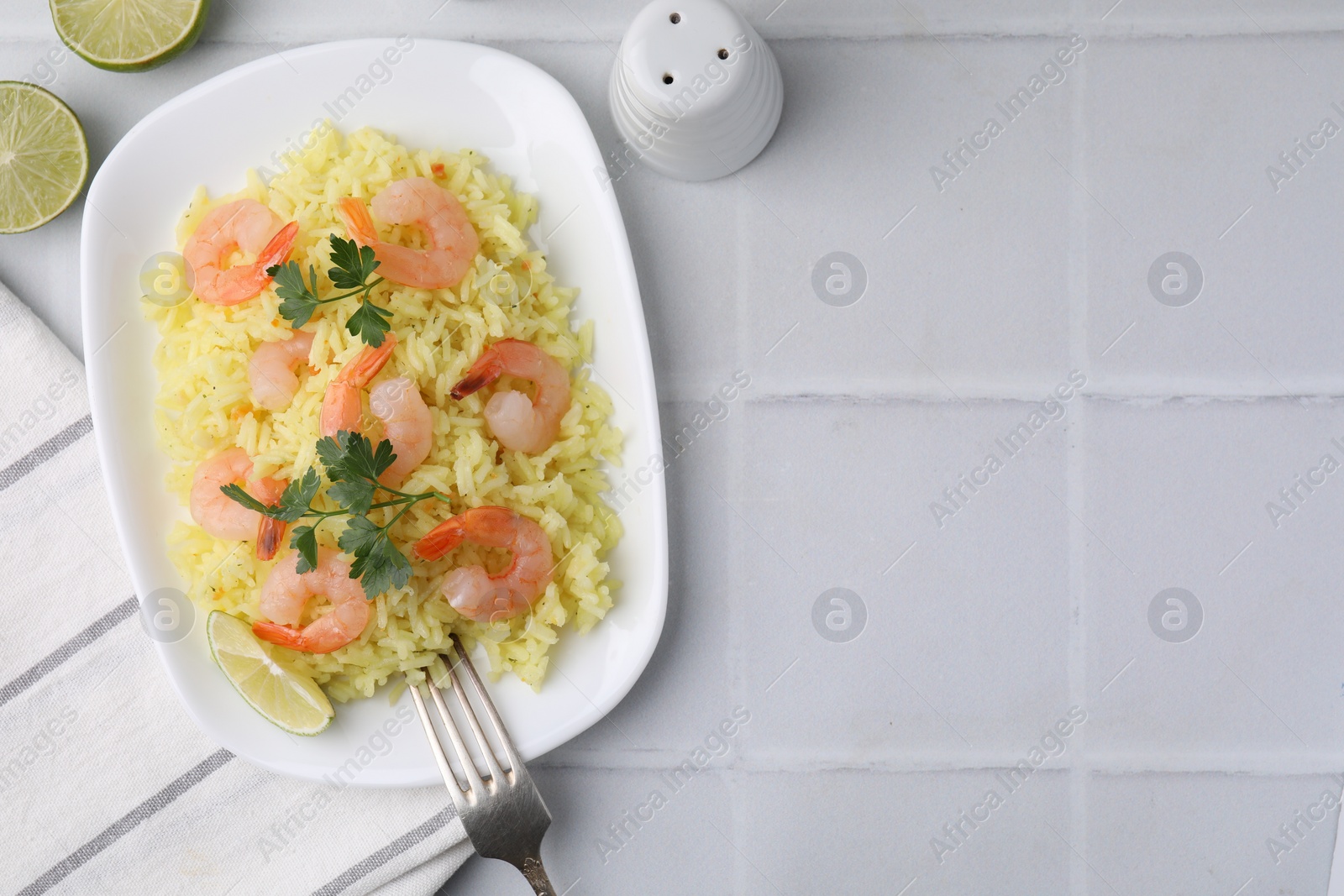 Photo of Delicious risotto with shrimps, lime and parsley on white tiled table, flat lay