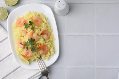 Delicious risotto with shrimps, lime and parsley on white tiled table, flat lay