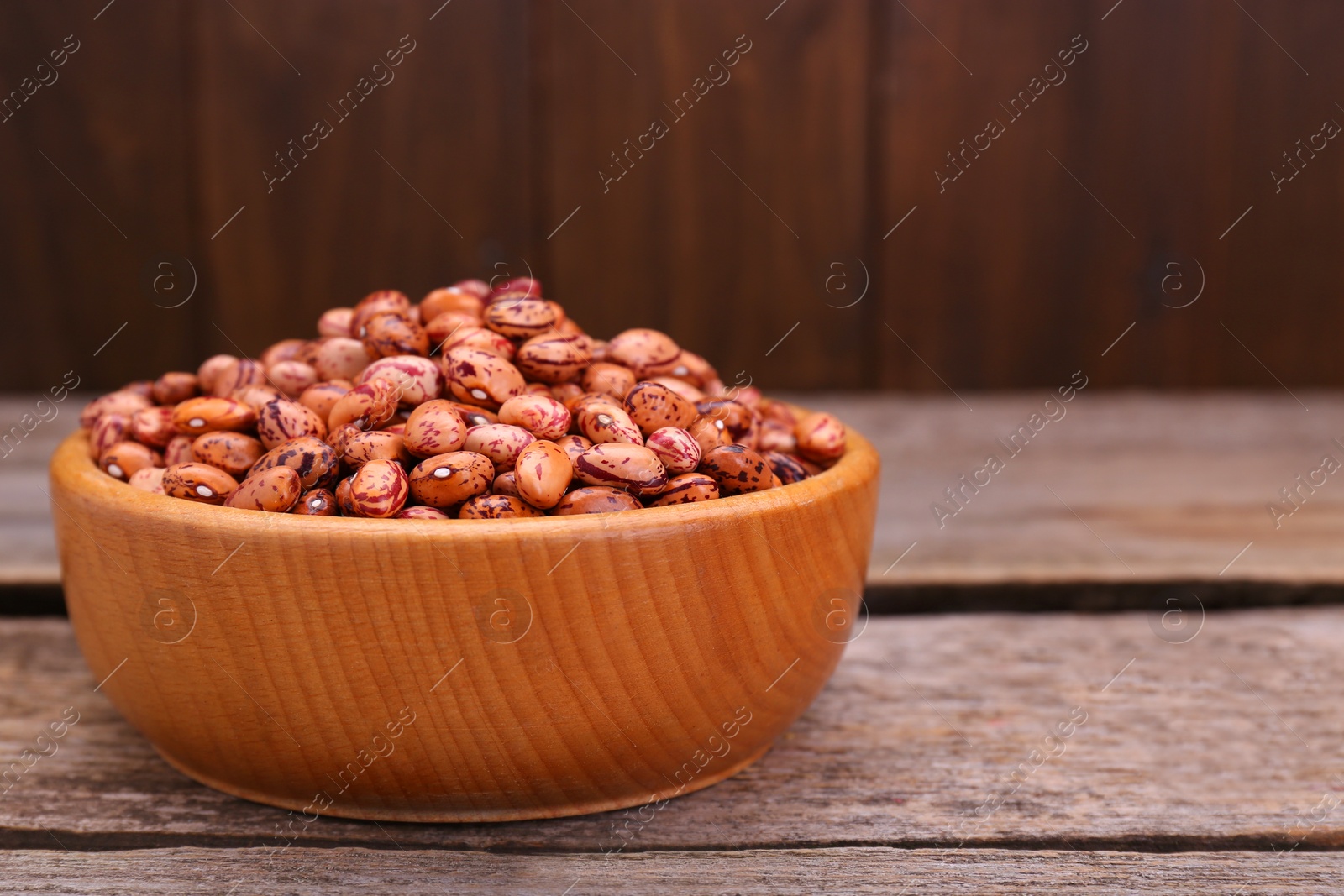 Photo of Bowl with dry kidney beans on old wooden table, closeup. Space for text