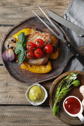 Photo of Delicious grilled meat and vegetables served with sauces on wooden table, flat lay