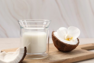 Photo of Glassdelicious vegan milk, coconut pieces and flower on white wooden table
