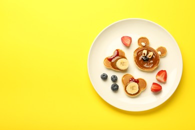 Photo of Creative serving for kids. Plate with cute bears made of pancakes, berries, banana and chocolate paste on yellow background, top view. Space for text