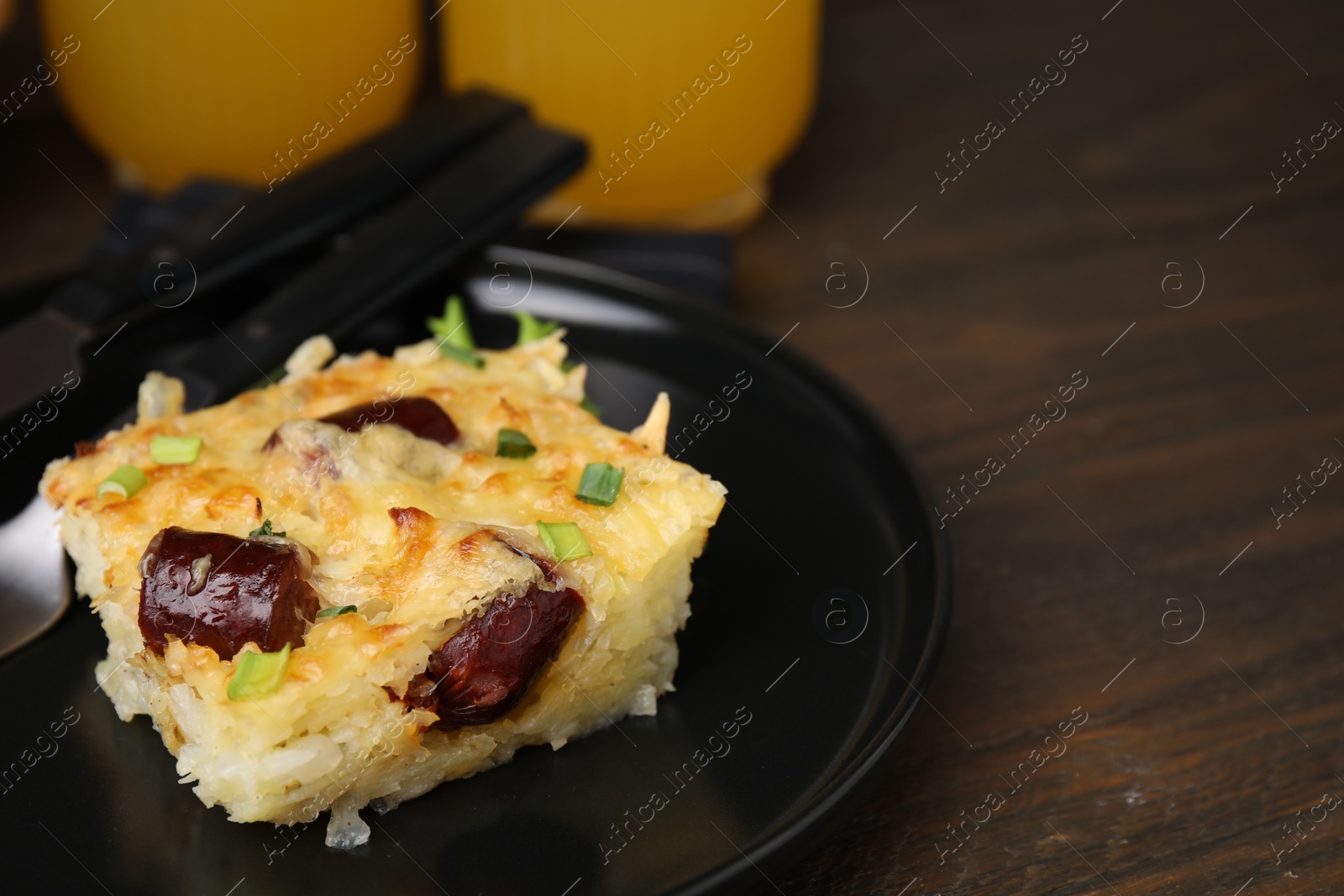 Photo of Tasty sausage casserole with green onions and cutlery served on wooden table, closeup. Space for text