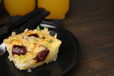 Photo of Tasty sausage casserole with green onions and cutlery served on wooden table, closeup. Space for text