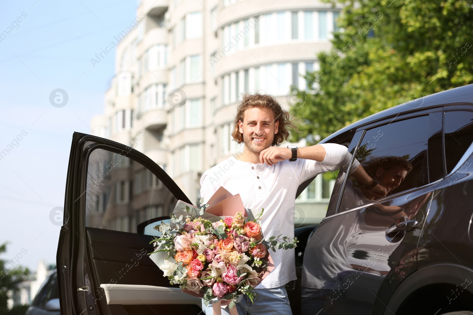 Photo of Young handsome man with beautiful flower bouquet near car on street