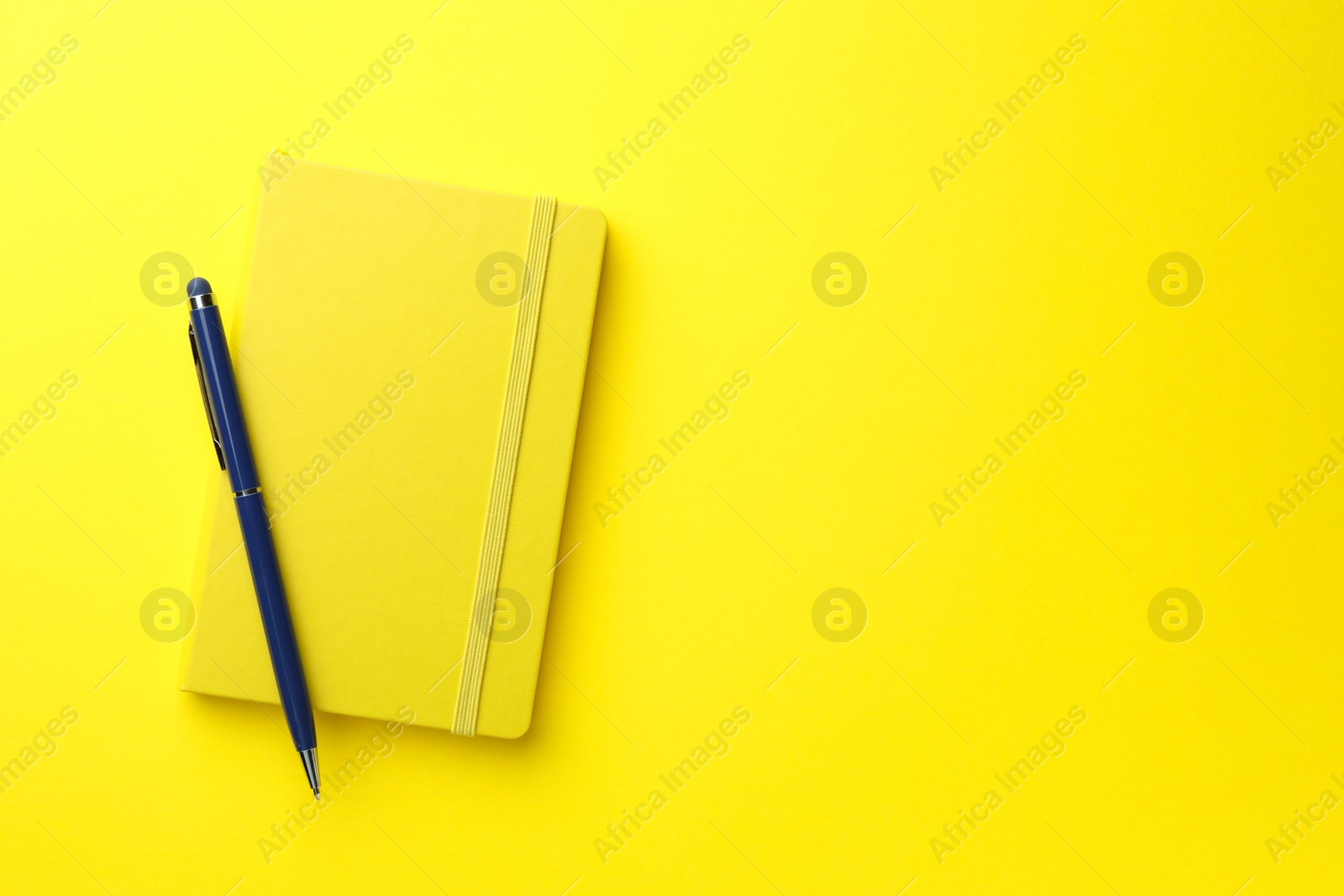 Photo of Closed notebook and pen on yellow background, top view. Space for text