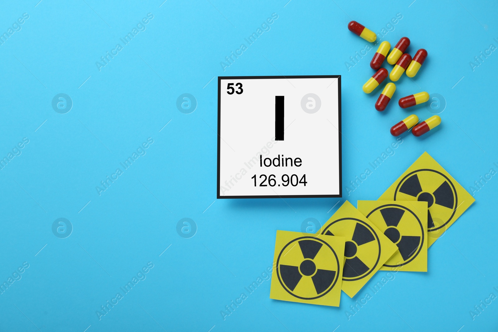 Photo of Card with chemical element Iodine, pills and radiation signs on light blue background, flat lay. Space for text