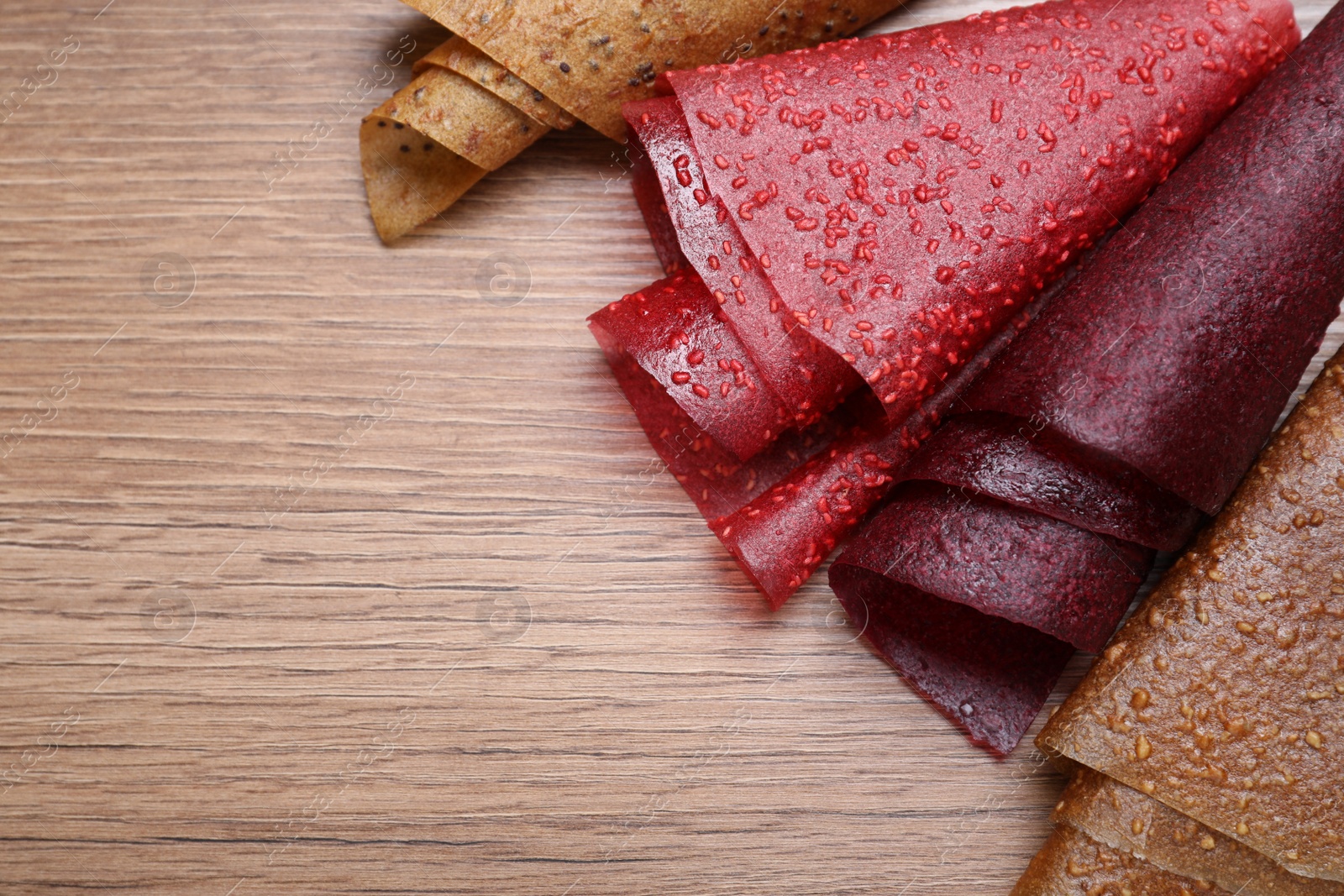 Photo of Delicious fruit leather rolls on wooden table, flat lay. Space for text