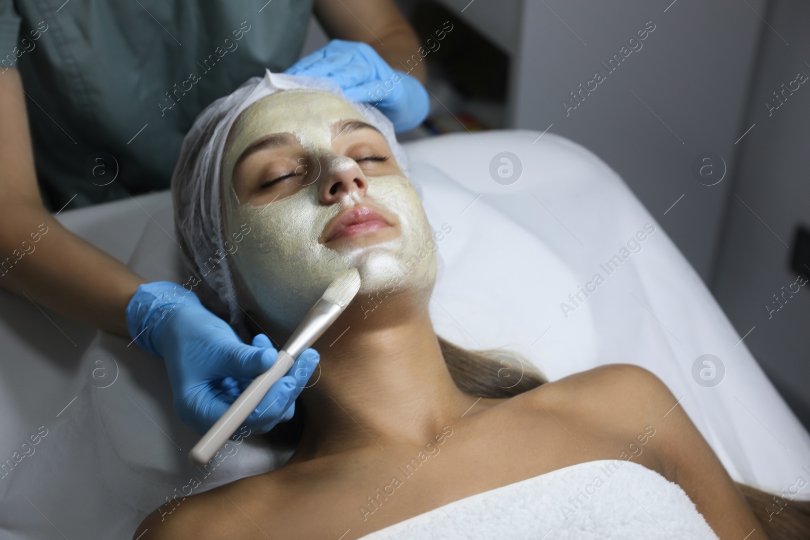 Photo of Cosmetologist applying mask on client's face in spa salon