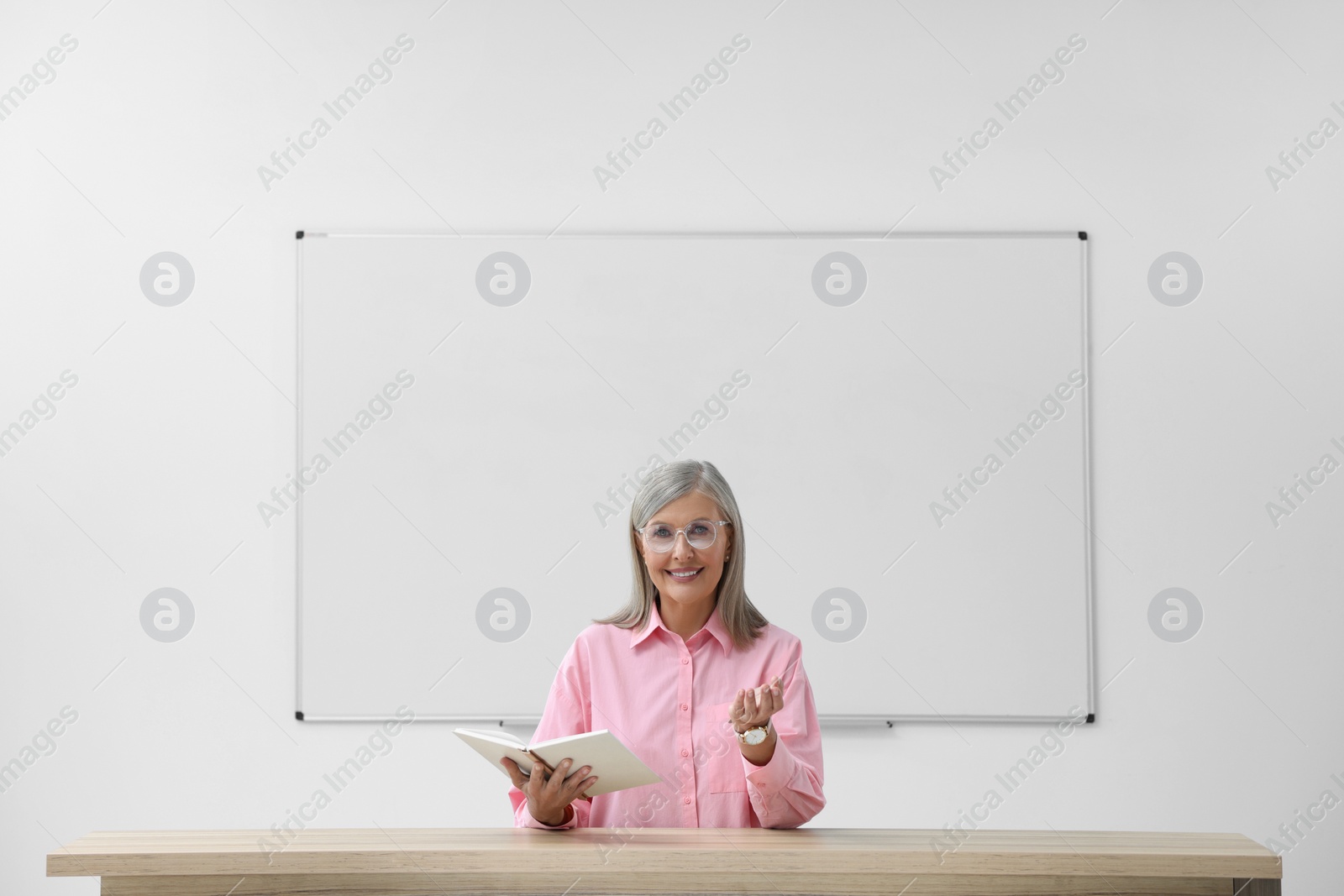 Photo of Happy professor with book giving lecture at desk in classroom