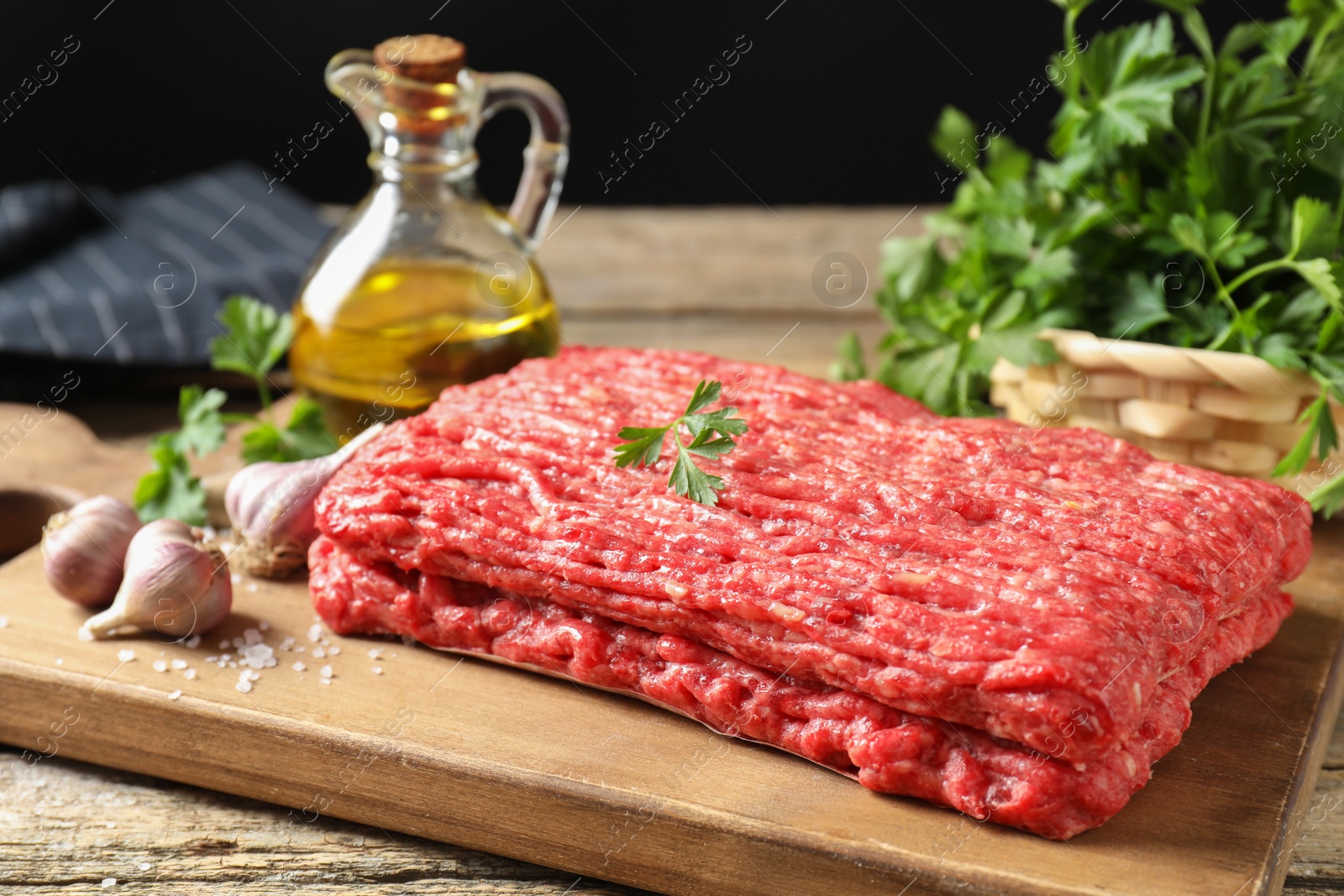 Photo of Raw ground meat, garlic, oil and parsley on wooden table