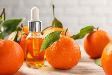 Bottle of tangerine essential oil and fresh fruits on white wooden table, closeup