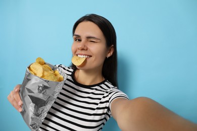 Photo of Woman taking selfie with potato chips on light blue background