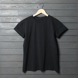 Hanger with stylish black T-shirt on gray wooden wall