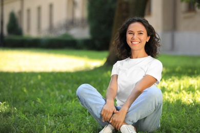 Photo of Happy young woman sitting on green grass in park on sunny day