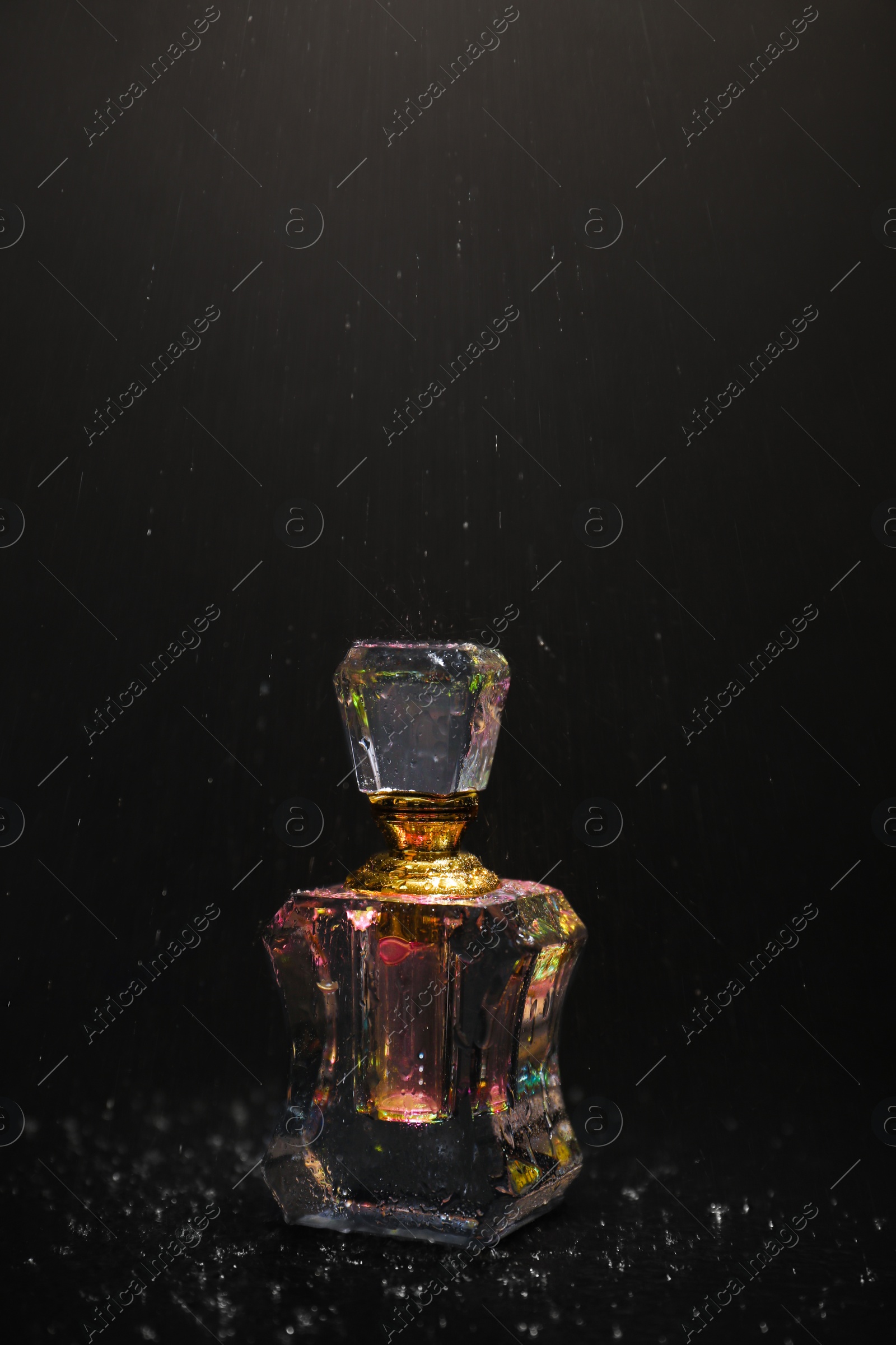 Photo of Falling water drops over perfume bottle on dark background