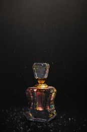 Photo of Falling water drops over perfume bottle on dark background