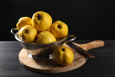 Tasty ripe quinces with water drops in metal colander and knife on black wooden table