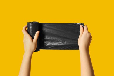 Woman holding roll of black garbage bags on orange background, closeup