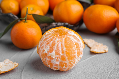 Photo of Peeled fresh ripe tangerine on grey table, closeup