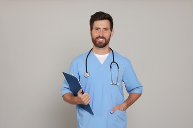 Photo of Happy doctor with stethoscope and clipboard on light grey background
