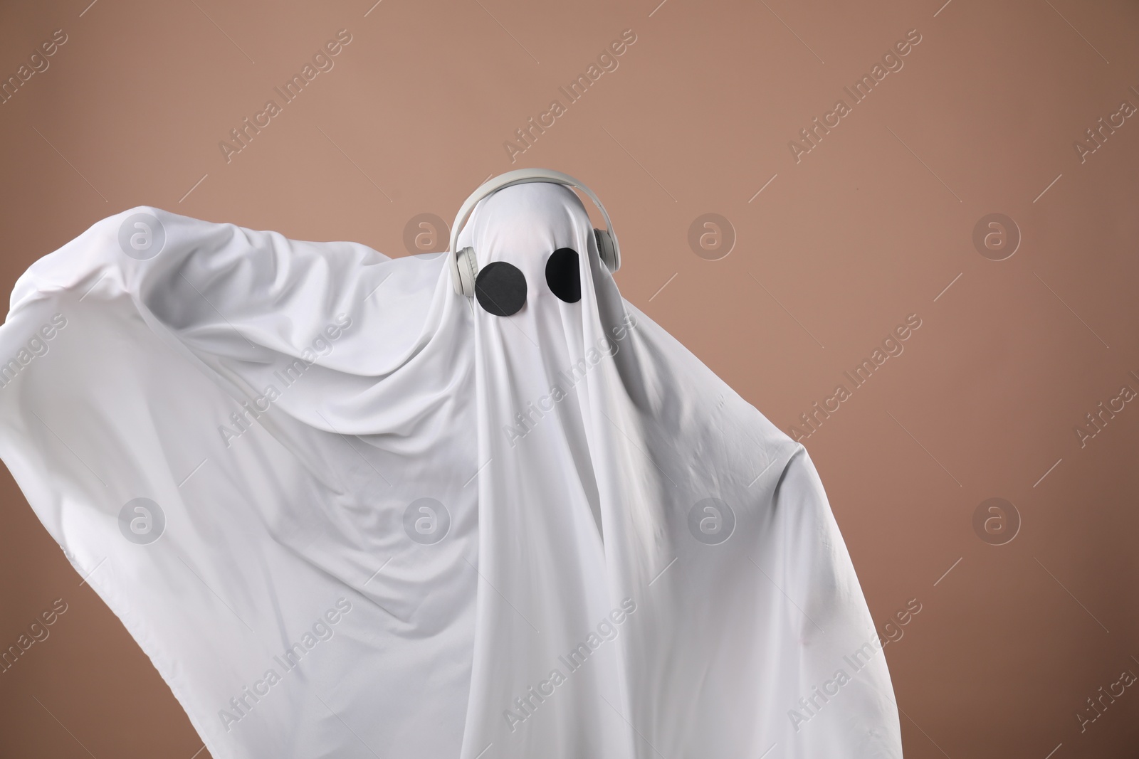 Photo of Person in ghost costume with headphones on dark beige background, space for text