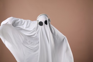 Person in ghost costume with headphones on dark beige background, space for text