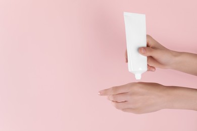 Photo of Woman applying cream onto hand on pink background, closeup. Space for text