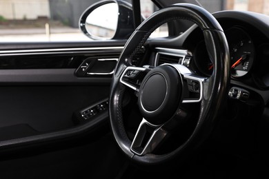 Steering wheel inside modern black car, closeup view