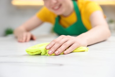Photo of Woman cleaning white marble table with rag in kitchen, closeup