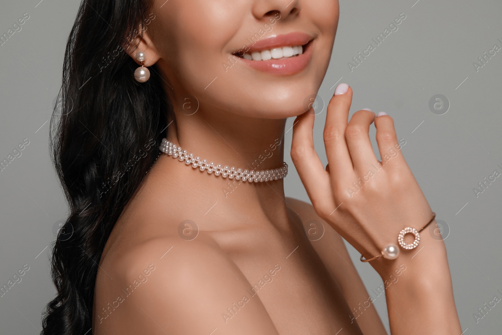 Photo of Young woman wearing elegant pearl jewelry on grey background, closeup