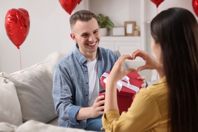 Photo of Man opening gift box from his girlfriend indoors. Valentine's day celebration
