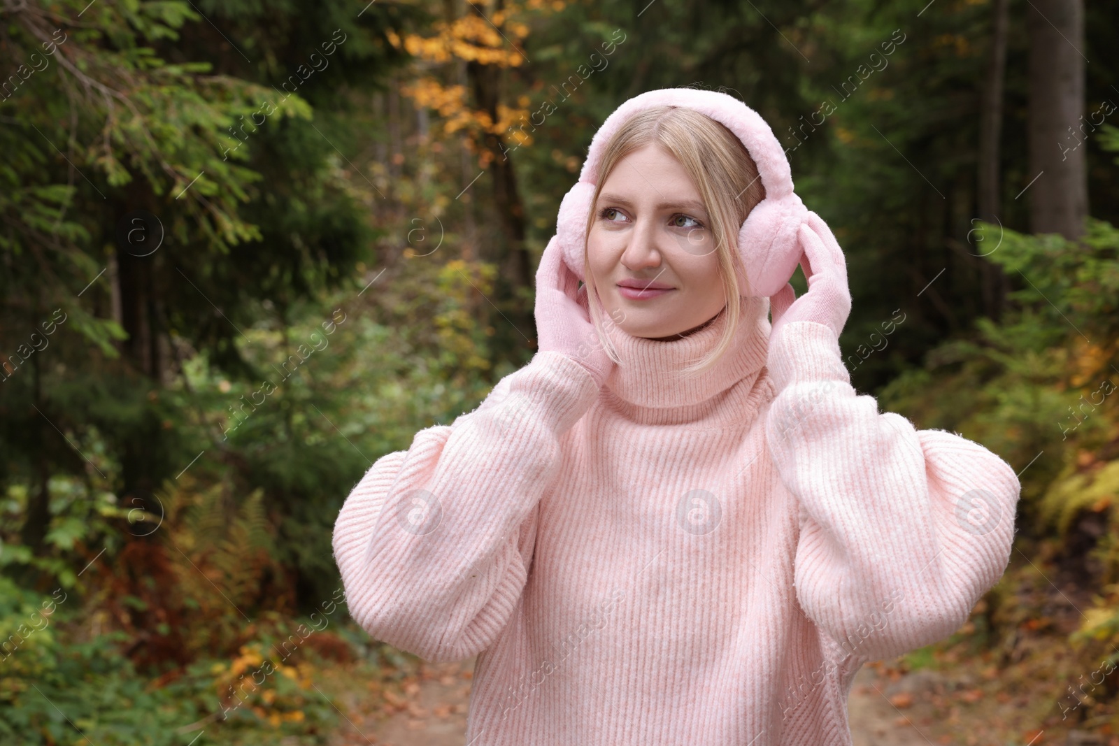 Photo of Young beautiful woman wearing warm earmuffs in forest