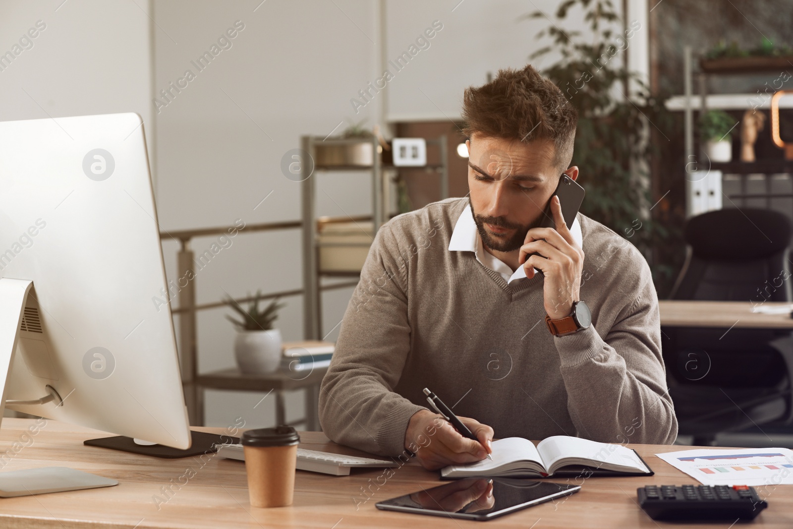 Photo of Man talking on phone while working at table in office